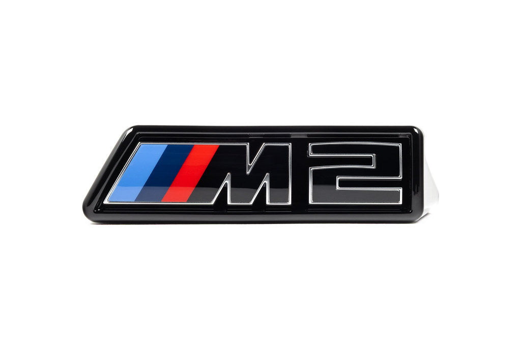 Alpha N G87 M2 LCI front grille emblem retainer with BMW OEM M2 badge on white background. Exterior car accessory.